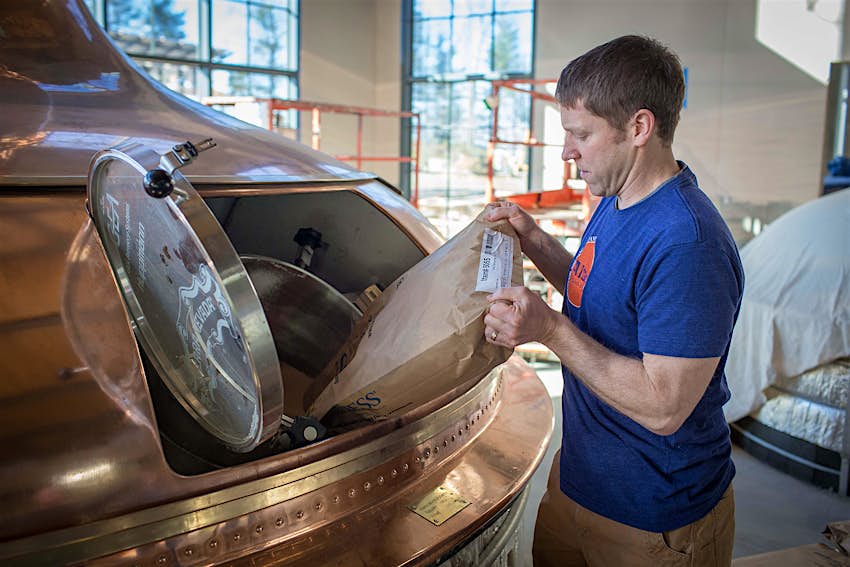 Man in blue shirt pours a sack of oats into an opening ina an old-fashioned copper still as part of the beer-making process. Craft breweries around the country take its products seriously. 