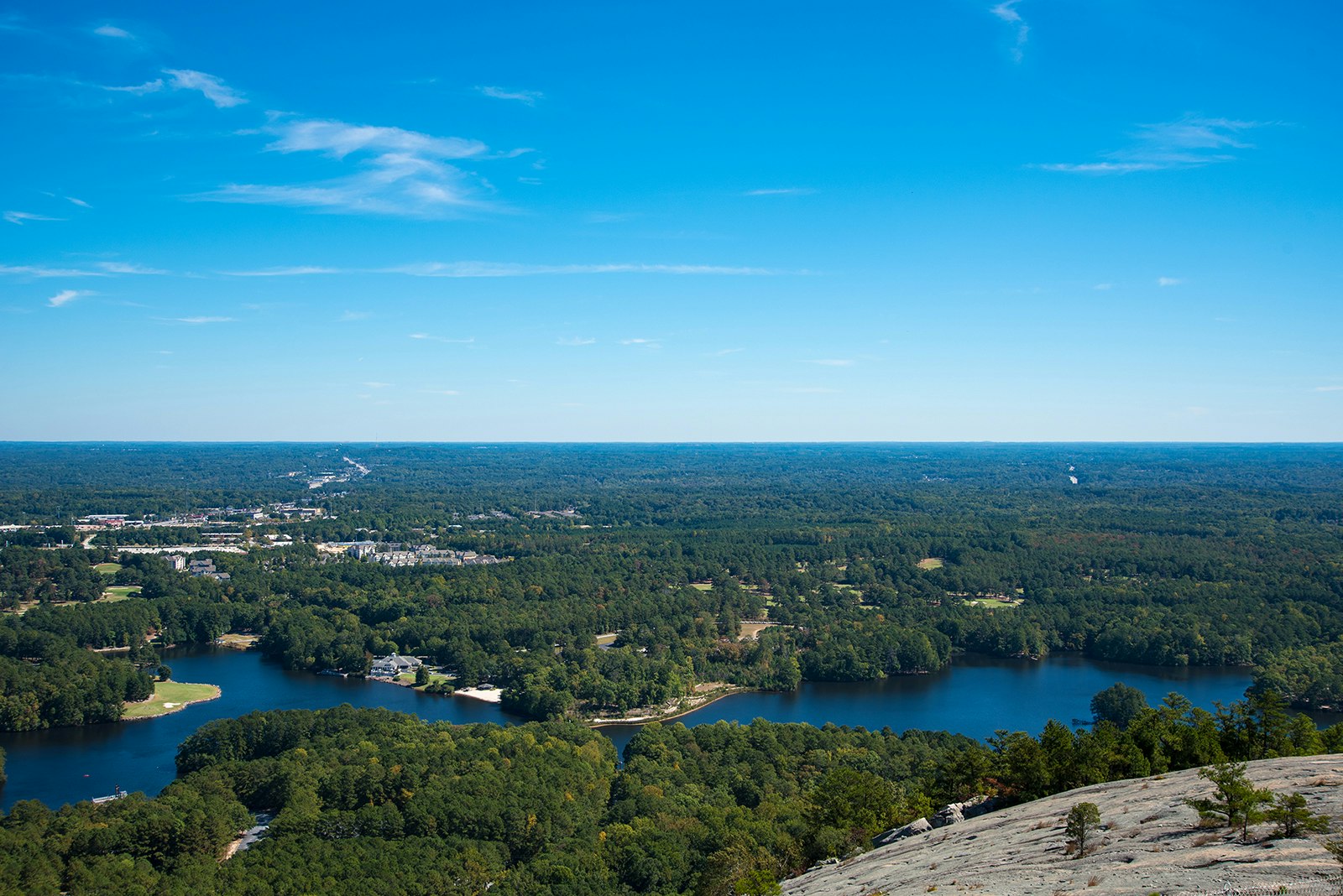 View on a clear, sunny day of the green trees and large blue lake at the foot of Stone Mountain, Georgia