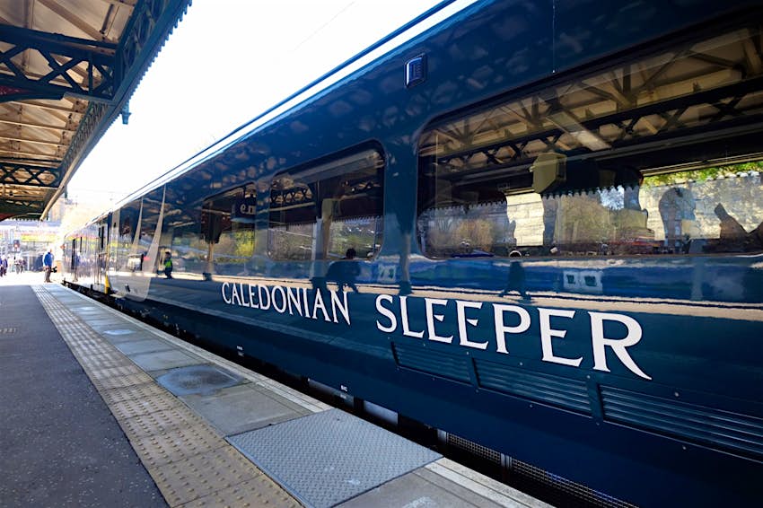 Features - Caledonian Sleeper stock A royal blue train sits in a station with the white logo of Caledonian Sleeper on the side; Amazing train journeys