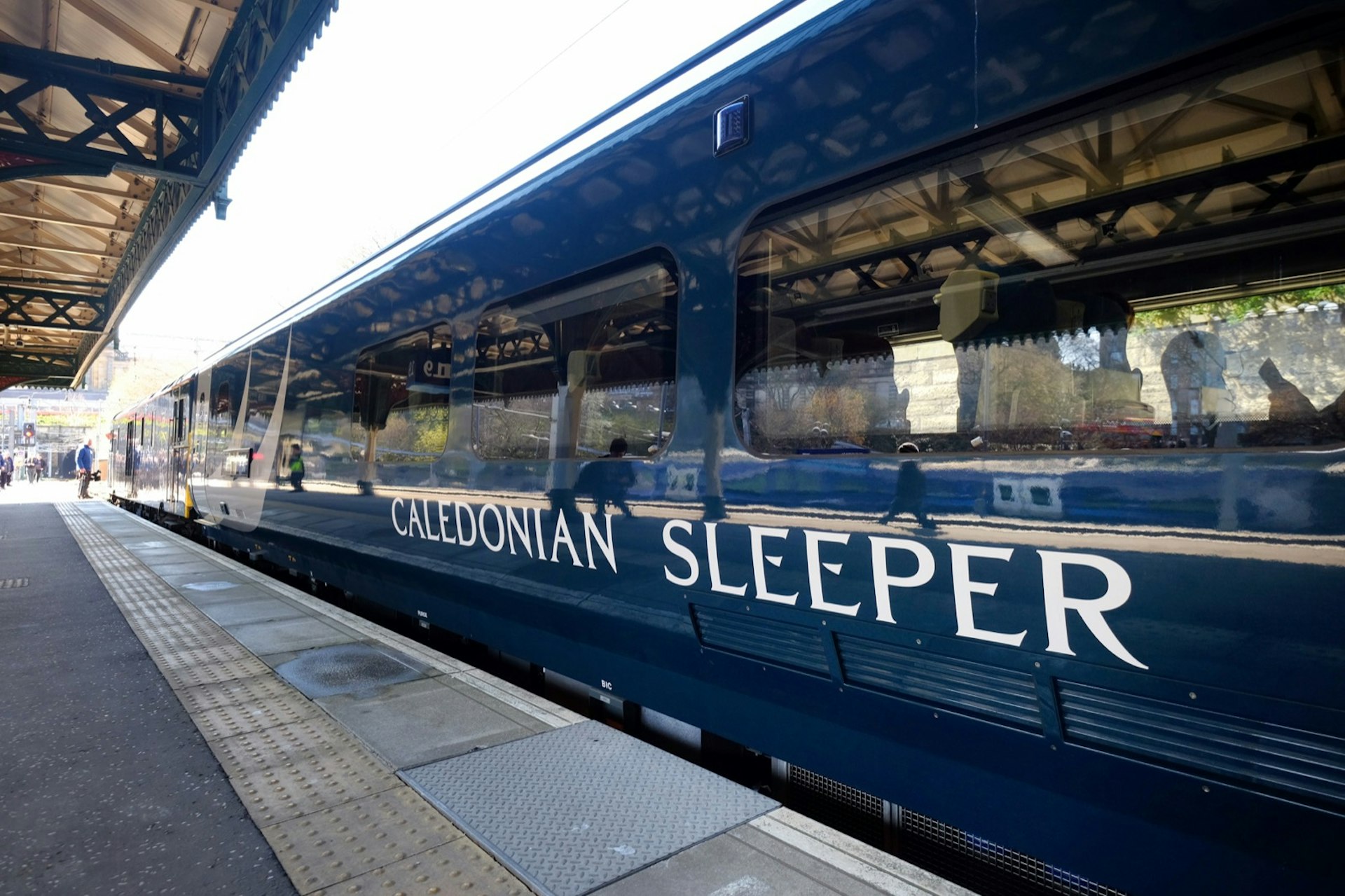 A royal blue train sits in a station with the white logo of Caledonian Sleeper on the side; Amazing train journeys