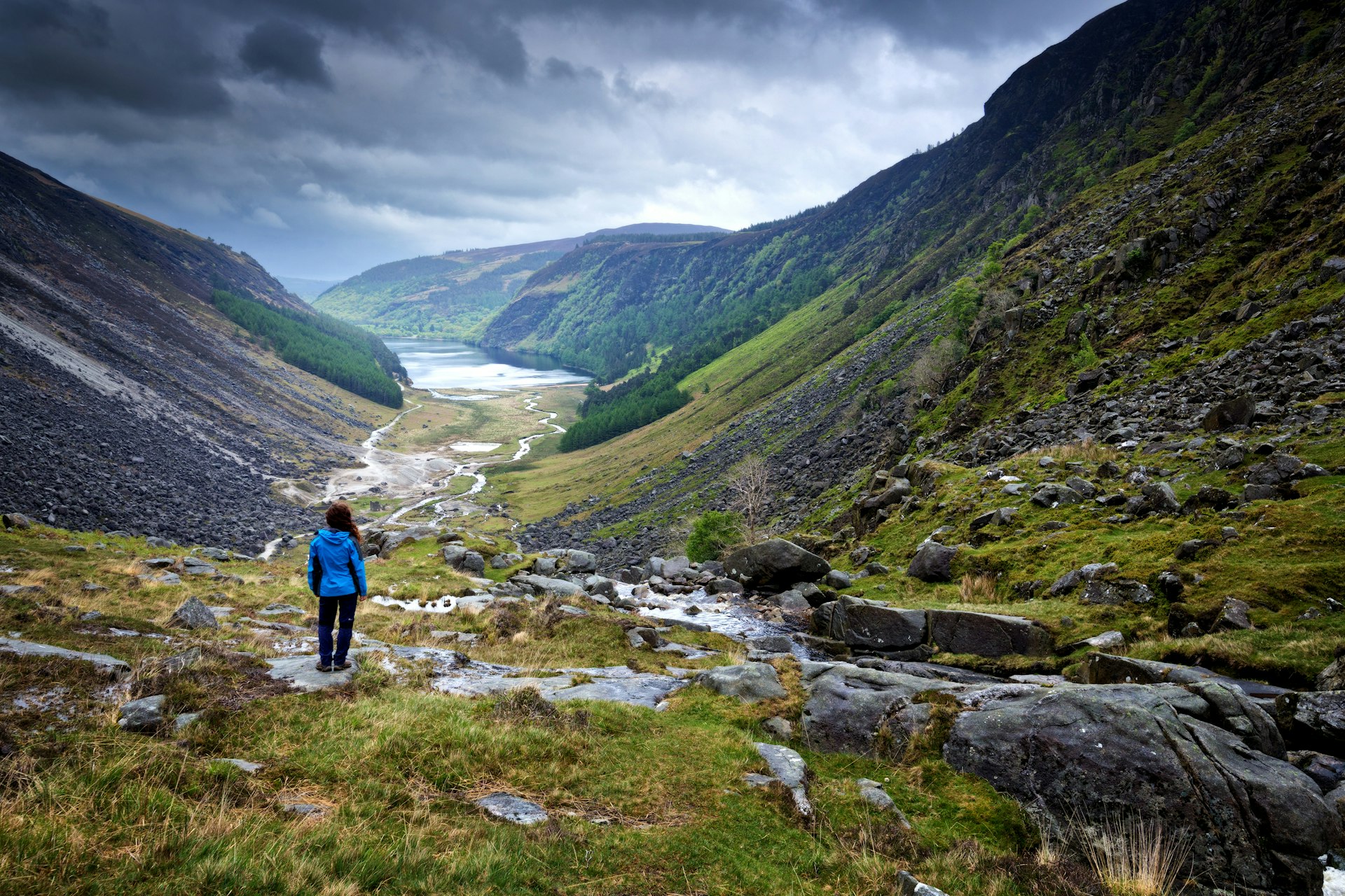 Features - Woman looking out on Glendalough Valley along Gleneaolo Valley walk in Wicklow Mountains, Ireland, stormy spring afternoon