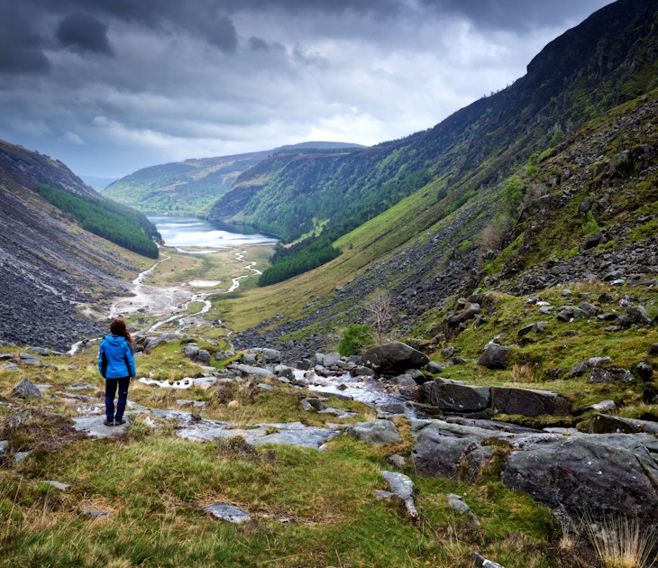 Features - Woman looking out on Glendalough Valley along Gleneaolo Valley walk in Wicklow Mountains, Ireland, stormy spring afternoon