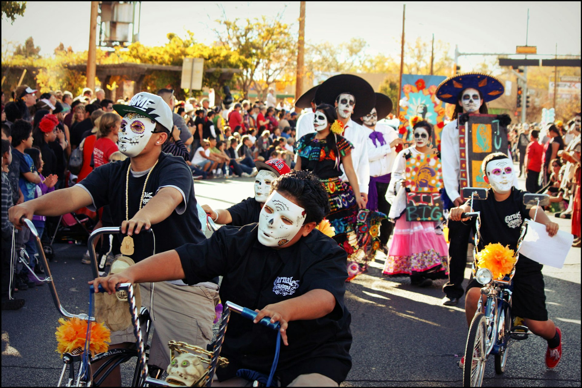 boys ride their bikes with their faces painted in the Calavera style in a parade
