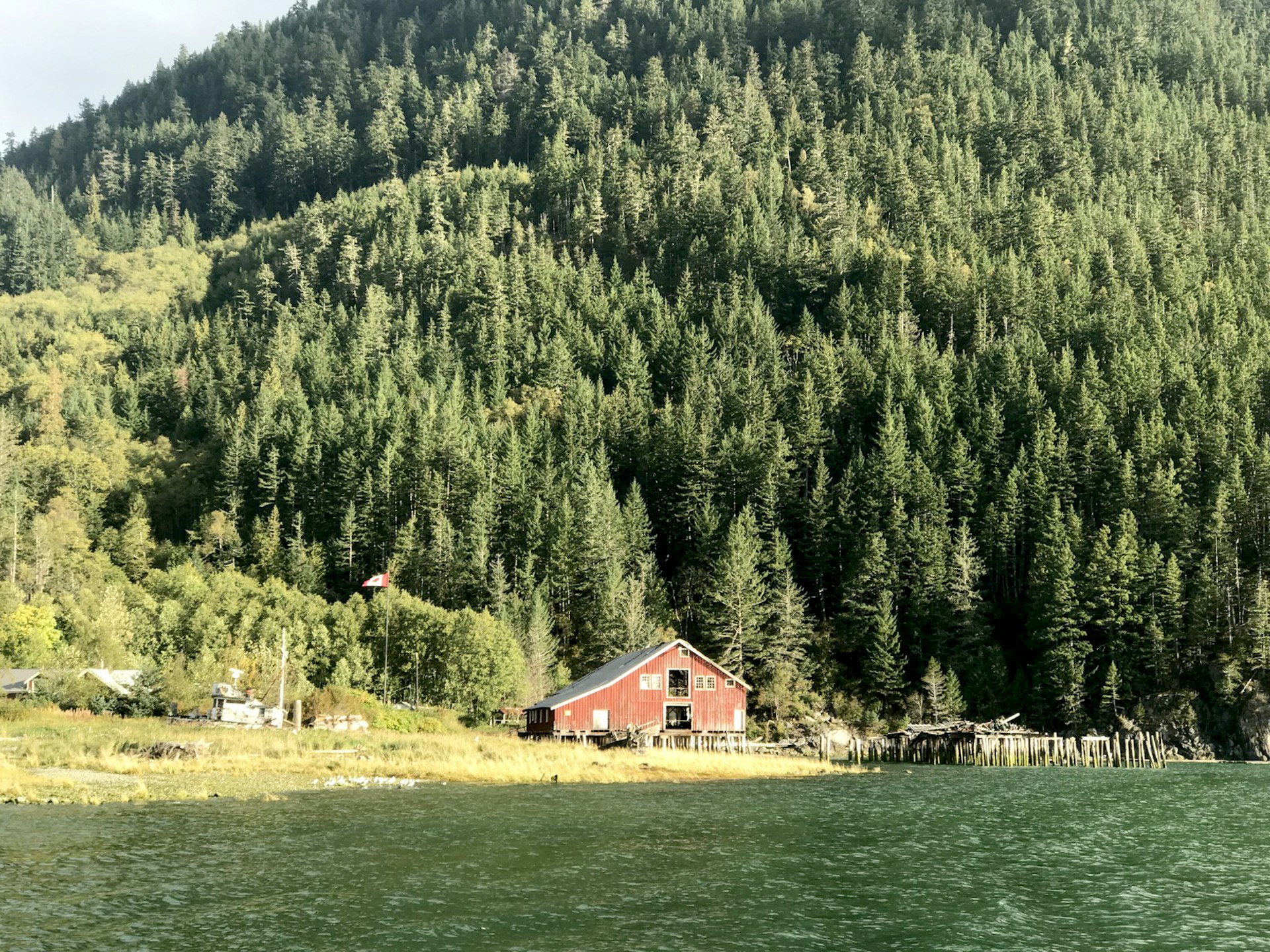 A dilapidated red-painted building and some old pilings stick out from a rugged coastline on the Inside Passage in British Columbia