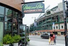 Exterior of Dutch & Doc's, a bar and restaurant, with Wrigley Field in the background and a woman and a child on the sidewalk