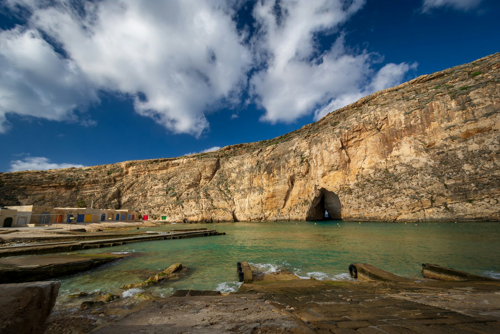 Looking across the turquoise waters of the small Inland Sea the cave entrance to the Med is visible at the base of the rock cliff. Colouful boat houses sit on the shore to the left © Geo-grafika / Getty Images