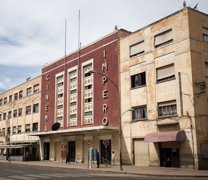 Flanked by two bland, sand-coloured buildings is the red, sleek-looking Cinema Imperio. Above the cantelevered cement awning that runs the length of the building are three symetrical rows of window climbing vertically up the building. On one side of them 'CINEMA' is written vertically in bold gold letters, on the other side is 'IMPERIO' © Stephen Lioy / Photography and Travel Media