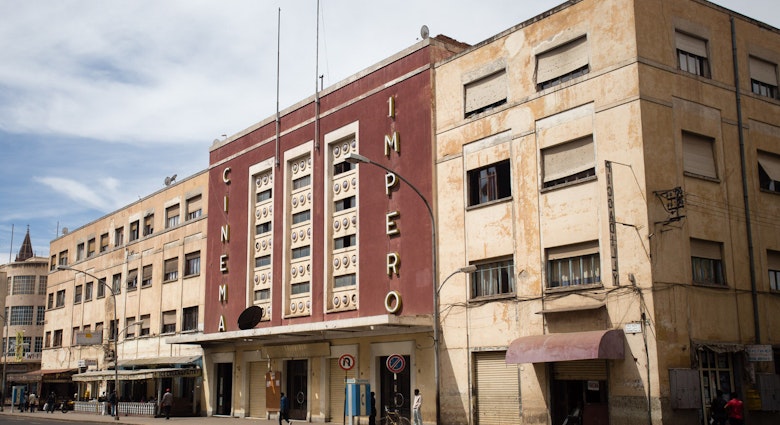 Flanked by two bland, sand-coloured buildings is the red, sleek-looking Cinema Imperio. Above the cantelevered cement awning that runs the length of the building are three symetrical rows of window climbing vertically up the building. On one side of them 'CINEMA' is written vertically in bold gold letters, on the other side is 'IMPERIO' © Stephen Lioy / Photography and Travel Media