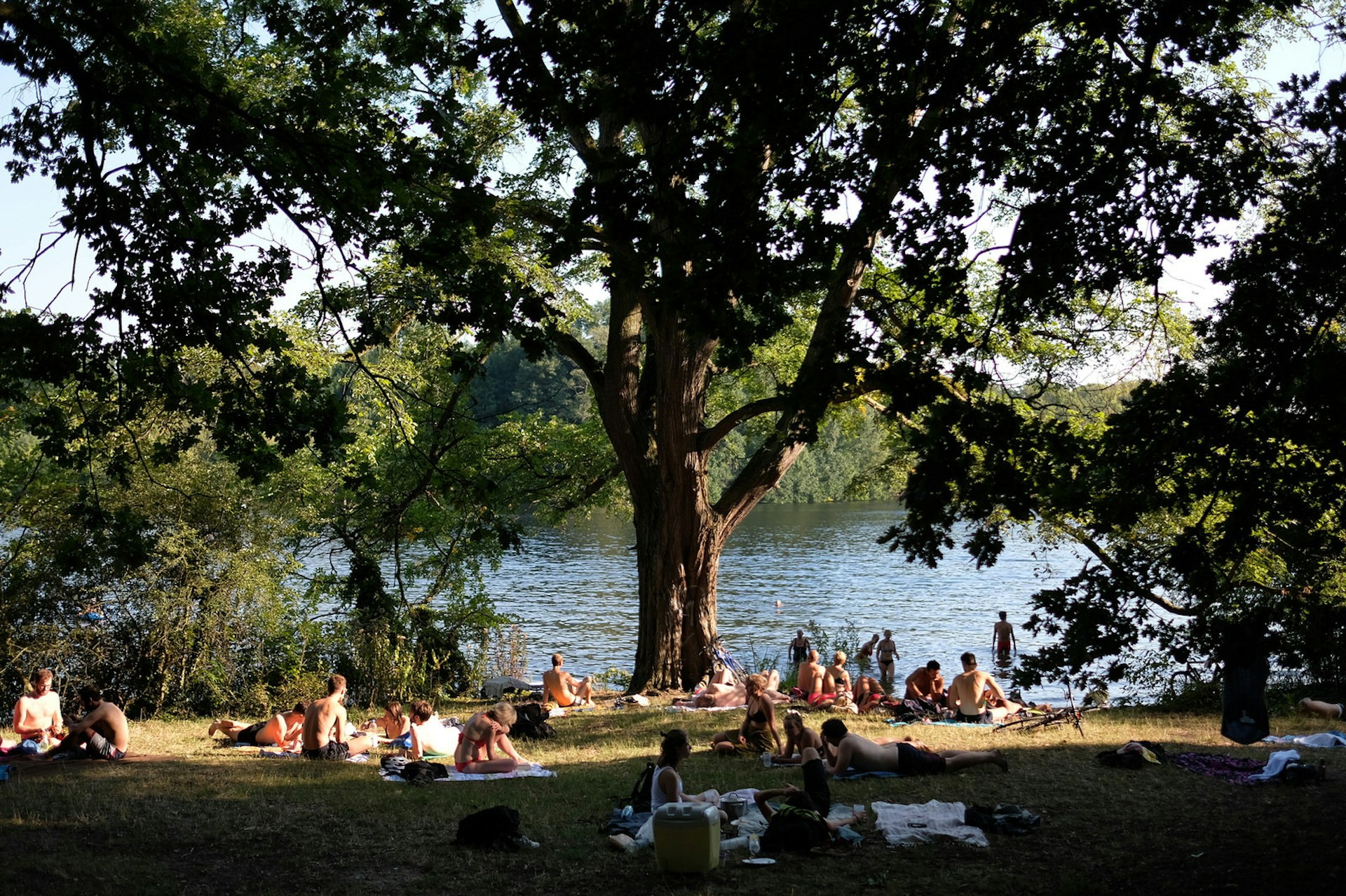 Free Berlin - People enjoying the hot summer weather at Tegeler See lake in Berlin, Germany. People lie on blankets in and out of the shade and a few are paddling in the lake