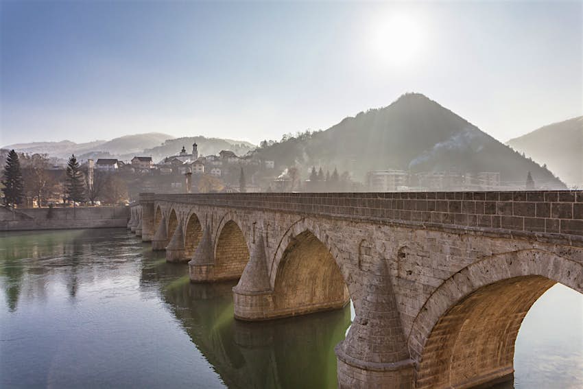 The symmetrical arches of the Mehmet Paša Sokolović Bridge, with the town of Višegrad in the background, shrouded in mist