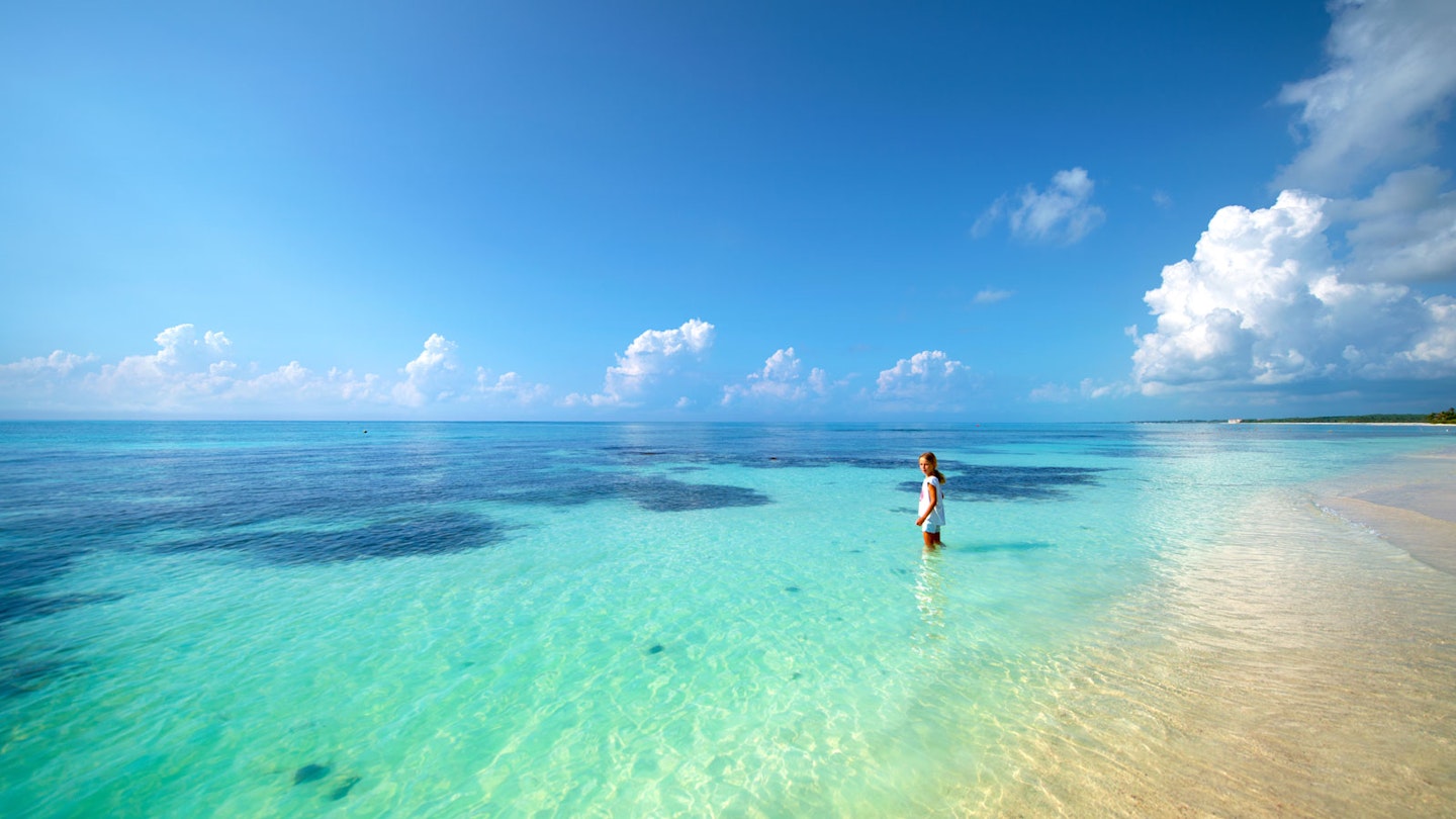 A girl stands in the shallow water of a turquoise ocean