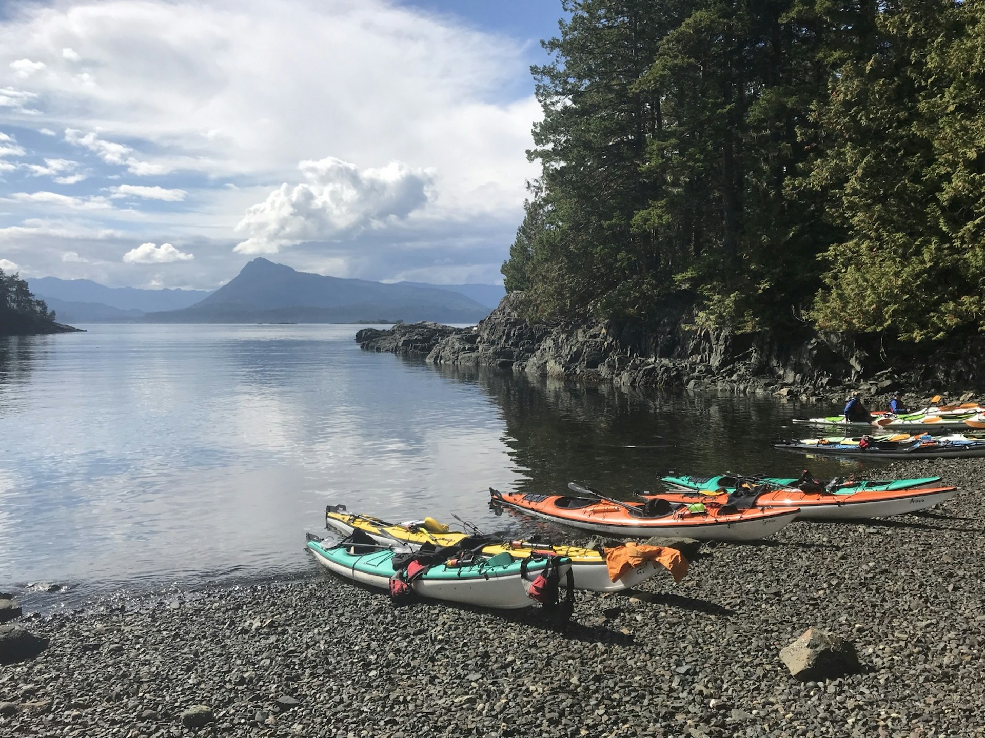 A row of kayaks are pulled onto a rocky beach as the beautiful scenery of British Columbia stretches out beyond.