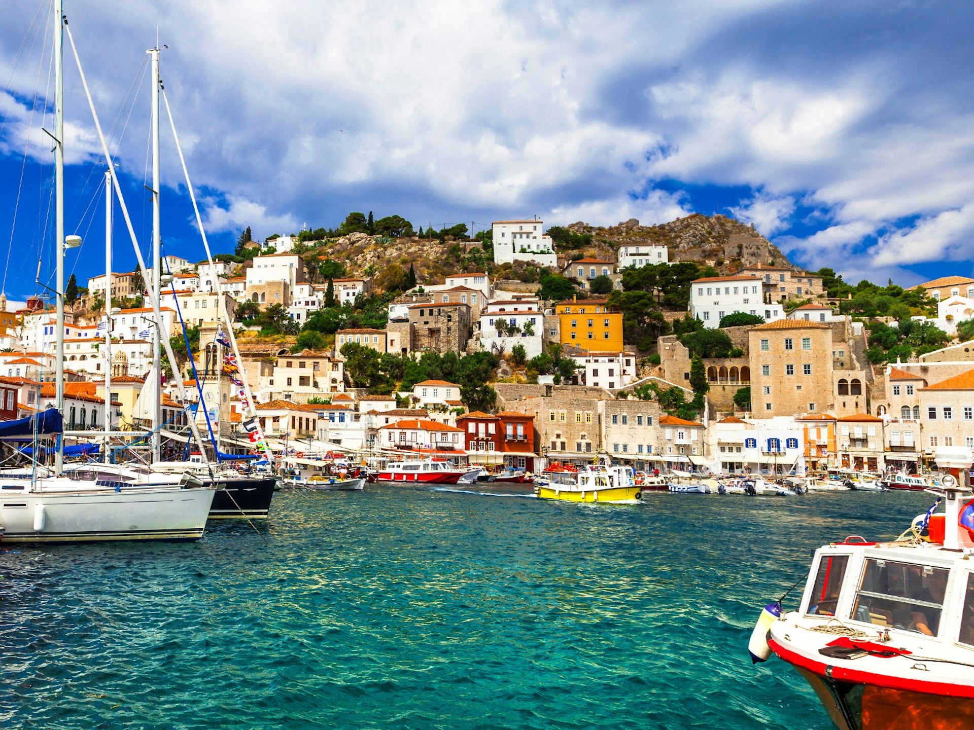 Fishing boats in the harbour at Hydra, with the town's houses huddled on a hillside behind them.