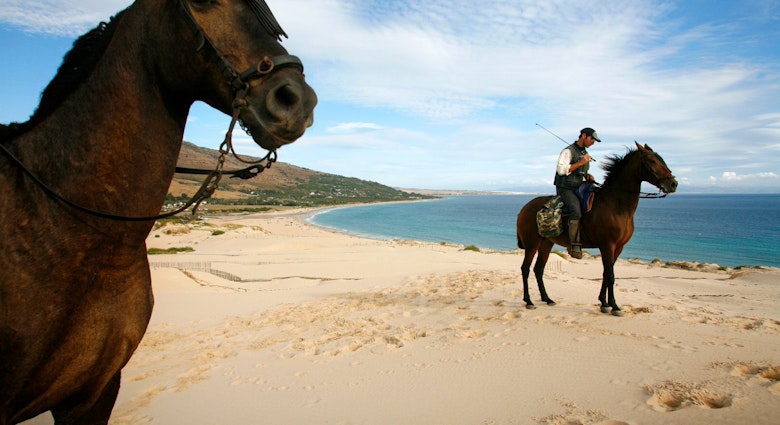 People riding horses on the dune of Ensenada de Valdvaqueros with a view over Playa de los Lances beach.