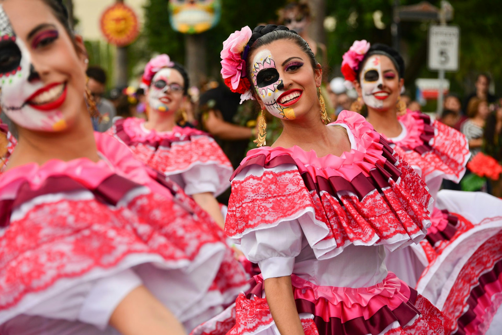 Women dance in pink and red traditional dresses their faces painted in the calavera style