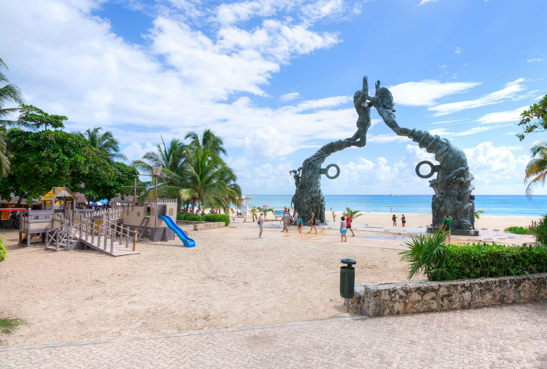 A mermaid statue serves as a gate to a pirate-themed playground on the beach