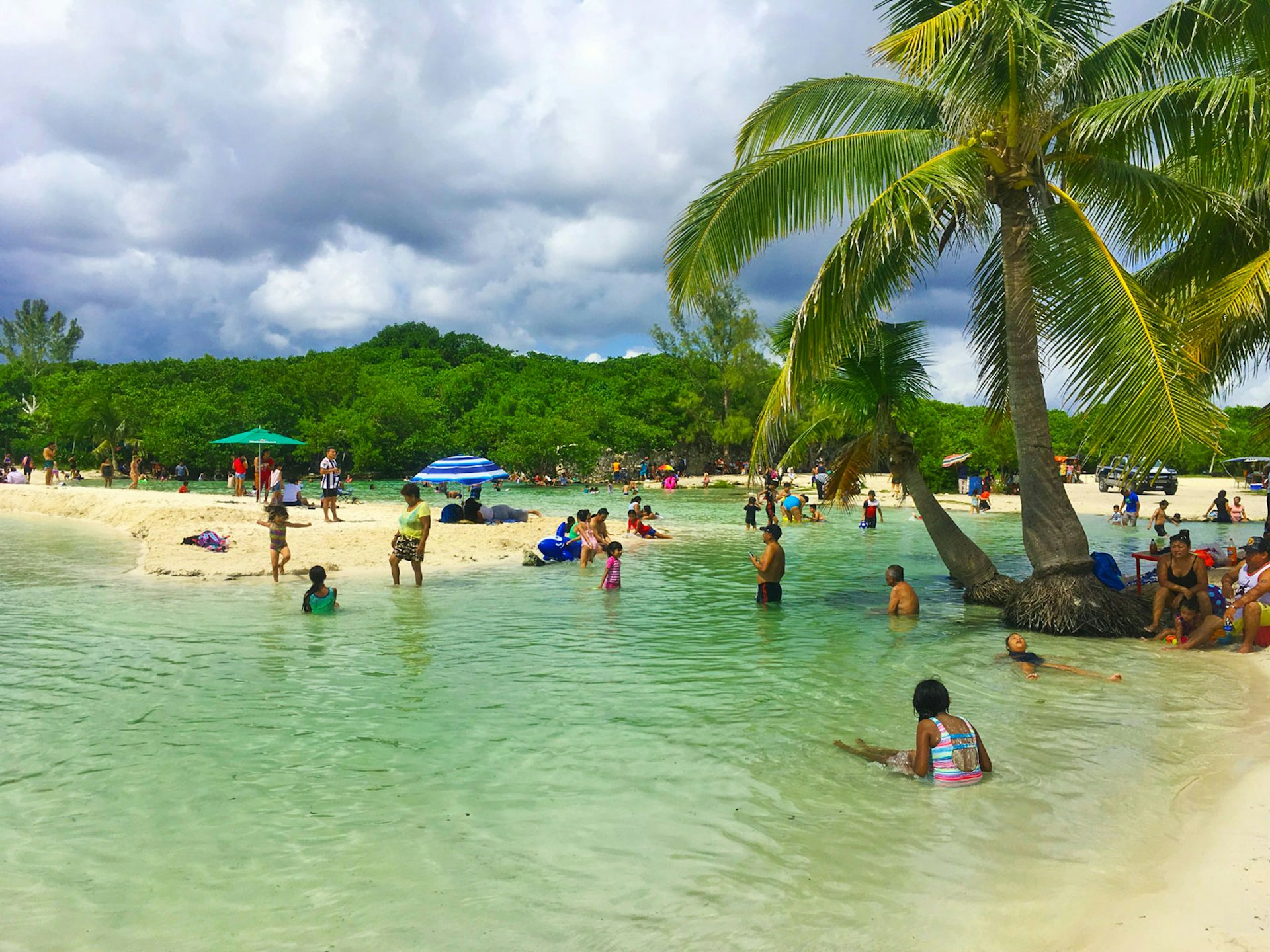 People enjoy the shallow water and white sand beach under palm trees