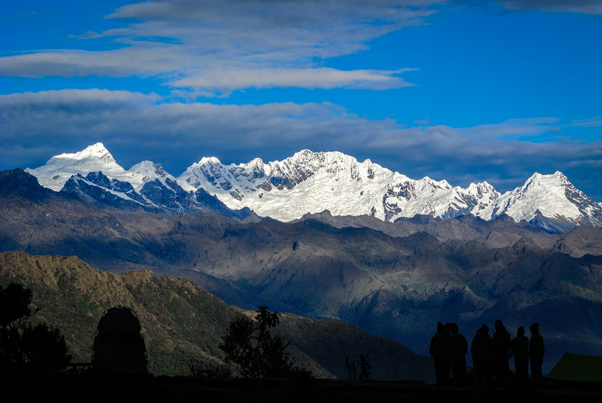 Porters and tourists silhouetted against a background of snowcapped mountains