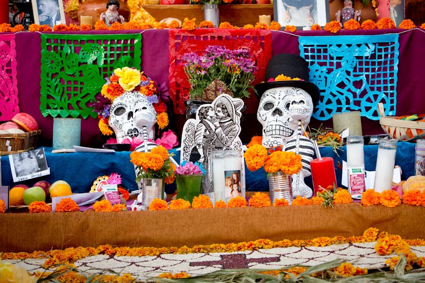 an ofrenda is covered with orange marigolds, candles, skulls and images of lost loved ones