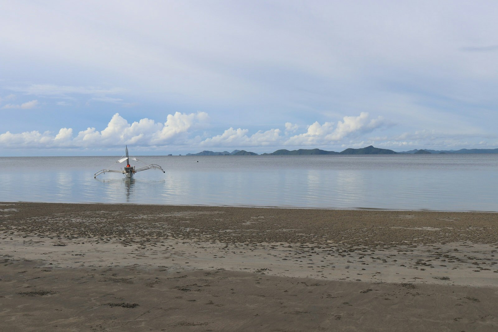 The islands of Linapacan are visible from the shore of a sandy beach on a sunny day