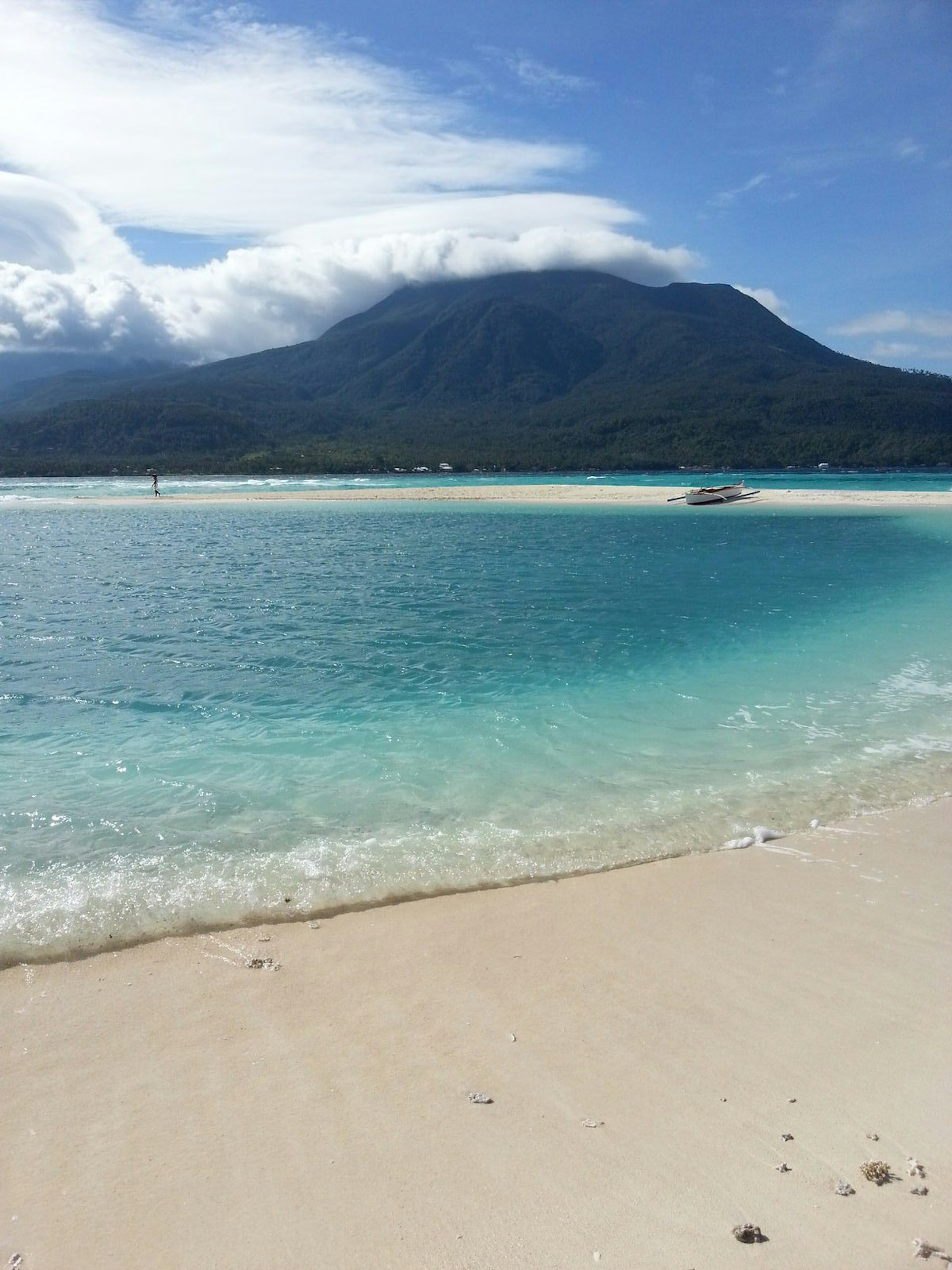 The imposing silhouette of Camiguin, topped with snow-white clouds, viewed from White Island. The land is seperated by a stretch of sparkling, turquoise water