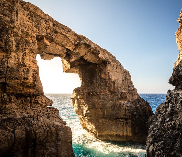 Sunlight bursts through a huge, angular rock arch on the coast of Goza at Wied il-Mielah. Wave surge between the two rock arms © Ramon Portelli / Getty Images