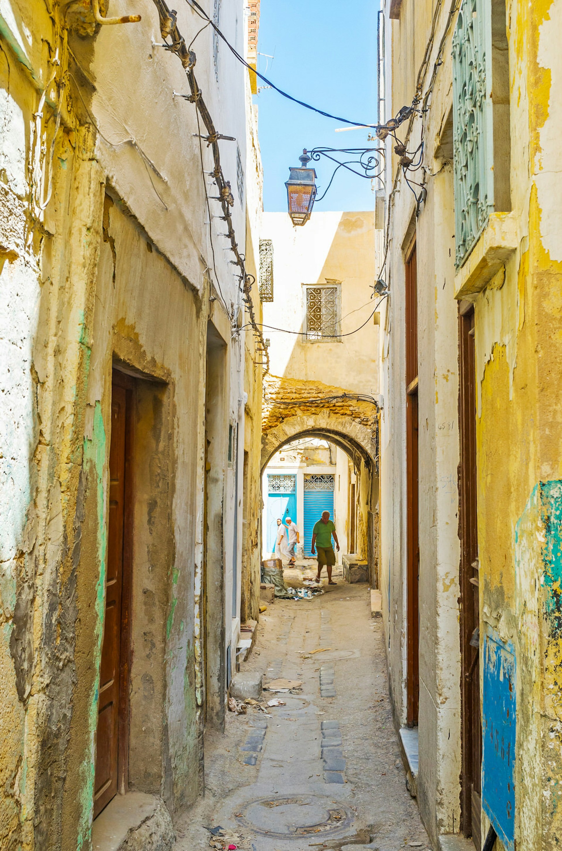Walking the old narrow streets of medina in Sfax, Tunisia, lined with shabby buildings of local workshops and houses.