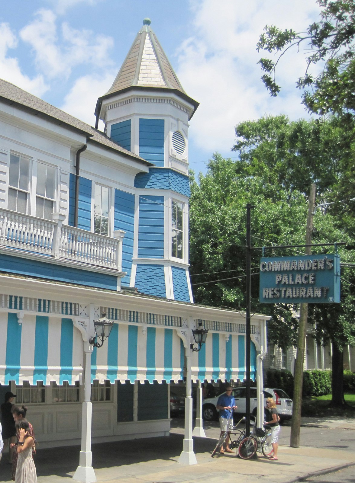 Exterior shot of Commander's Palace in New Orleans – a large, Victorian building painted turquoise blue with white trim – on a sunny day in the Garden District