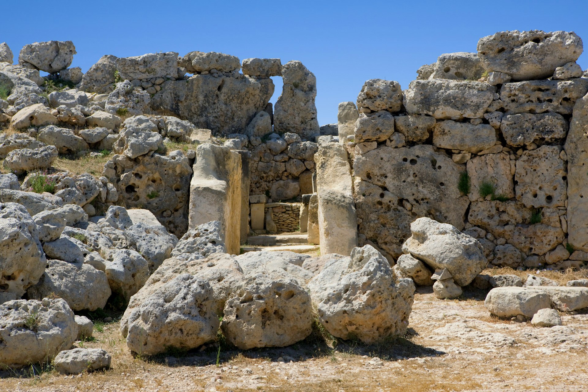 Large limestone boulders lay on the parched ground in front of the entrance to one of the Ġgantija Temples. Rough hewn slabs make up the outer walls, while the entrance is composed of two neatly carved monoliths © Jean-Pierre Lescourret / Lonely Planet