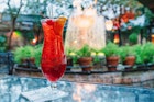 A bright red hurricane drink, served in a traditional tulip-shaped glass, on a table outdoors in a garden in the evening