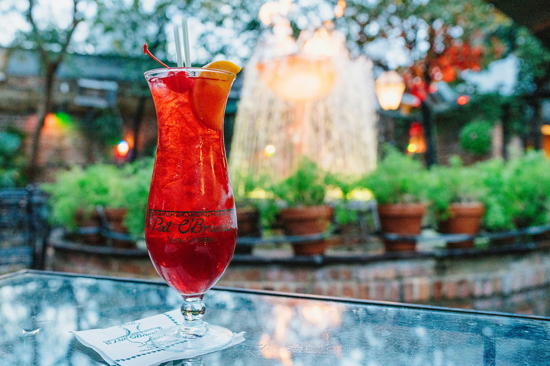 A bright red hurricane drink, served in a traditional tulip-shaped glass, on a table outdoors in a garden in the evening