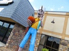 off-center photo of a statue of folk hero Johnny Appleseed, which stands 14ft tall. He's wearing blue pants, a yellow shirt and a frying pan hat – and he's carrying an apple.