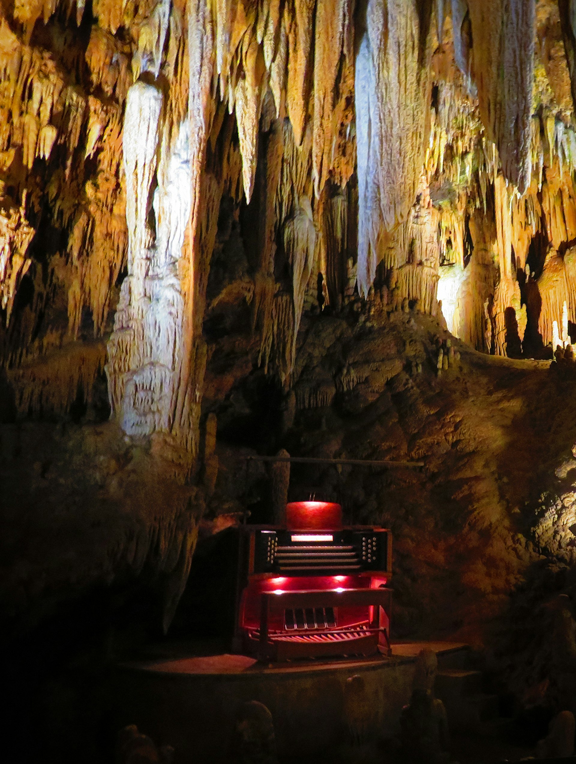 A small organ – which plays notes on stalactites – glows red and is framed by tan stalactites underground in Luray Caverns, Virginia