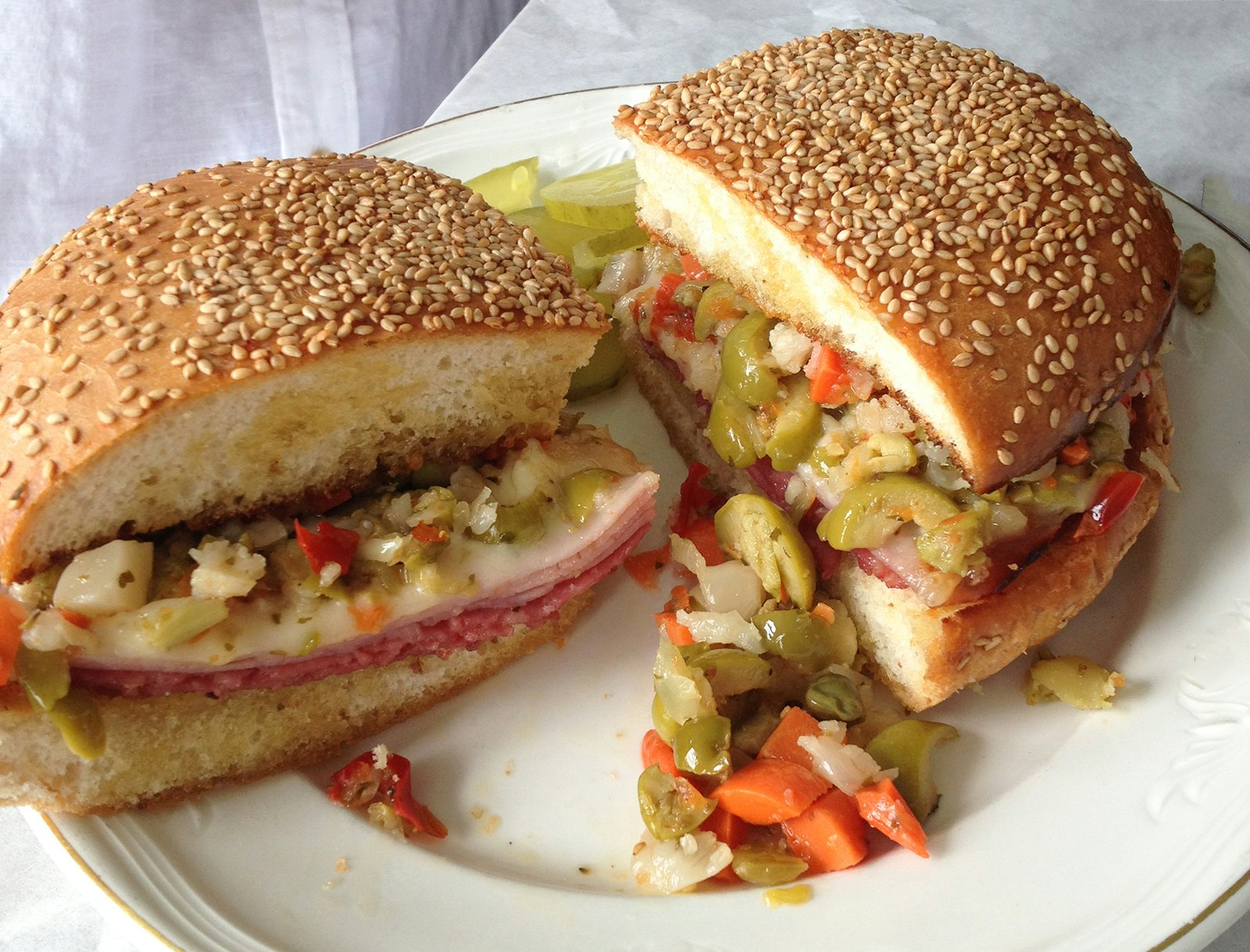 close-up of a muffuletta sandwich – piled with Italian meats and olive tapenade, on a sesame seed bun – on a white plate in New Orleans