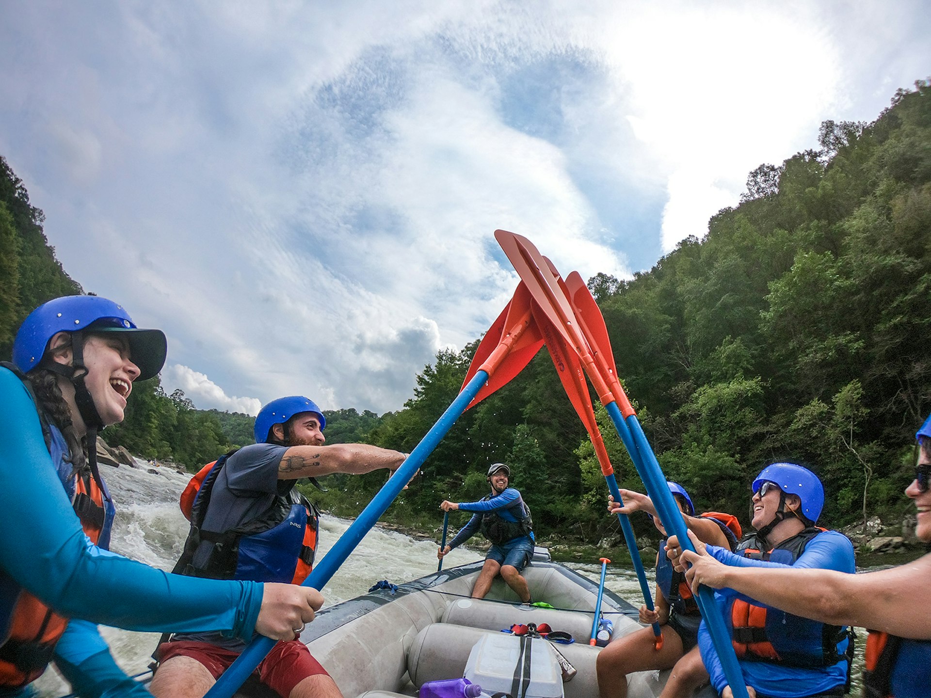 A man and four women raise their orange paddles into the air for a 'paddle high five' on the Gauley River in West Virginia, on a cloudy day