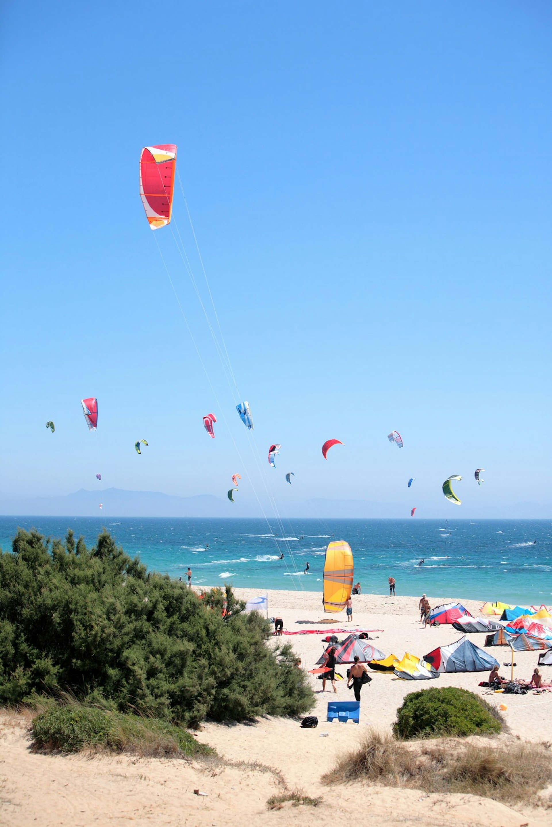 Tarifa beach packed with kite surfers and sunbathers, Colourful kites and tents stand out against the clear blue sky and white sand beach. 