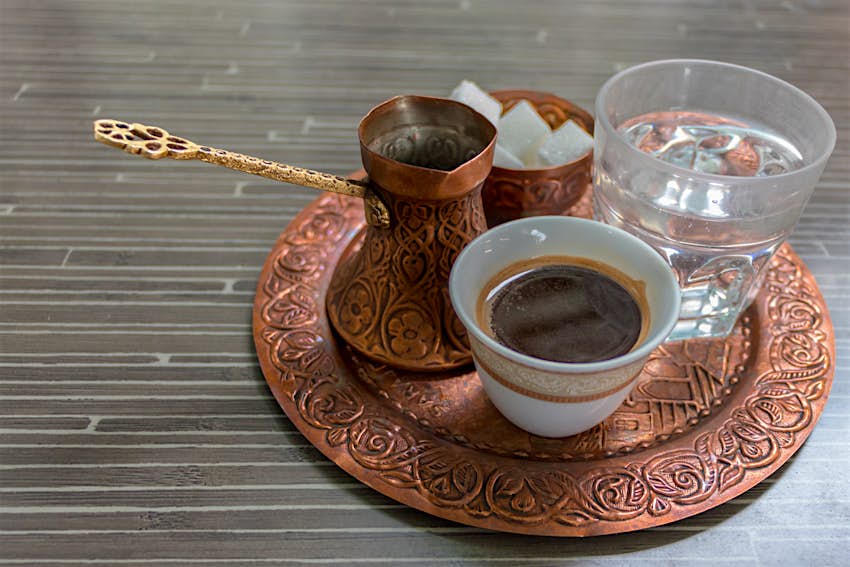 Features - shutterstock_1119648395-83f9f2a7096b A cup of traditional Bosnian coffee with a glass of water and sugar lumps