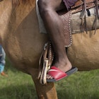 close up of saddled brown horse with a red slide sandal in the stirrups