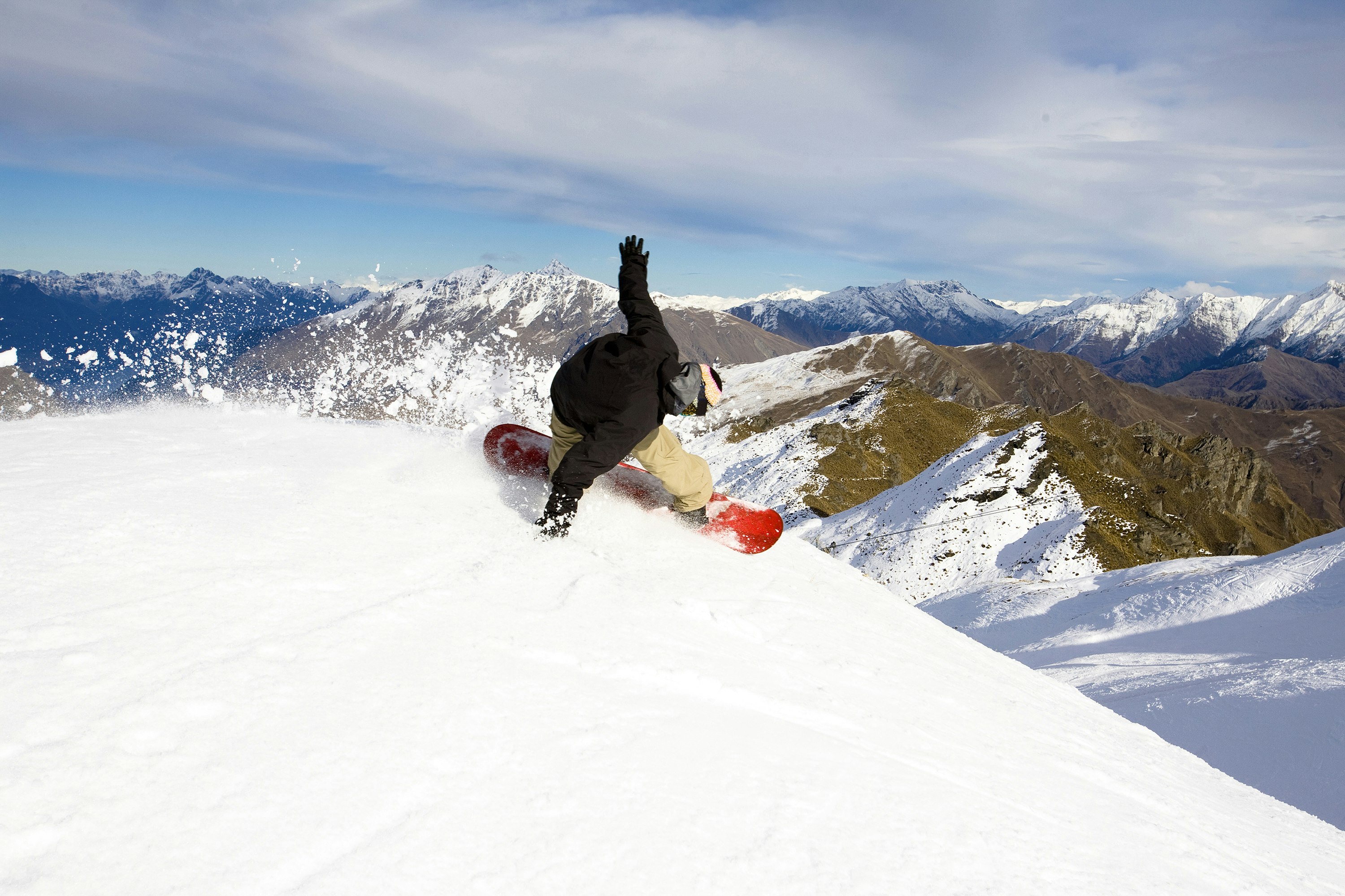 Features - A male snowboarder blasts a heel side turn while snowboarding at Coronet Peak in Queenstown, New Zealand.
