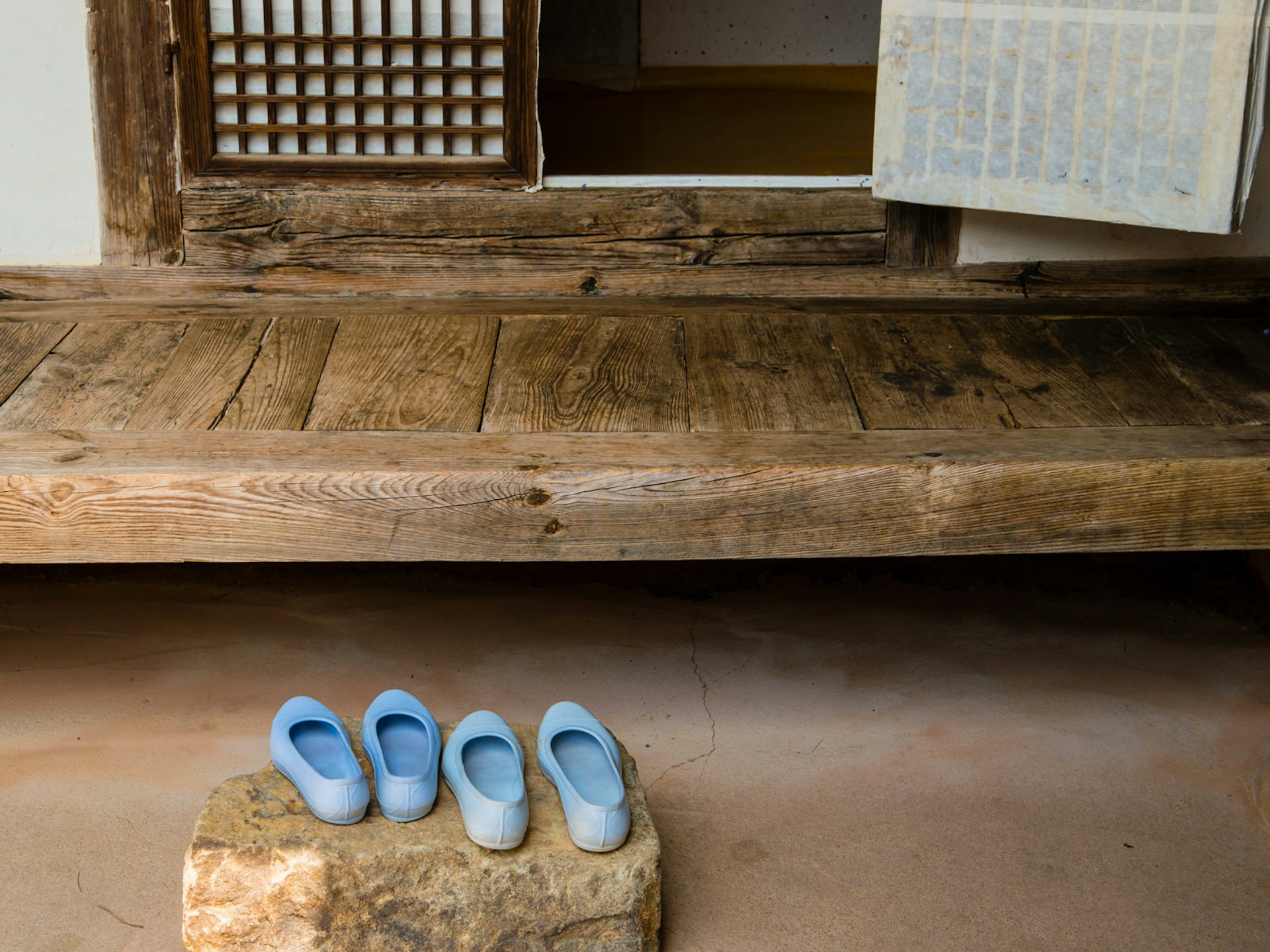 Two pairs of blue shoes left on a stone outside a wooden doorway to a traditional Korean home