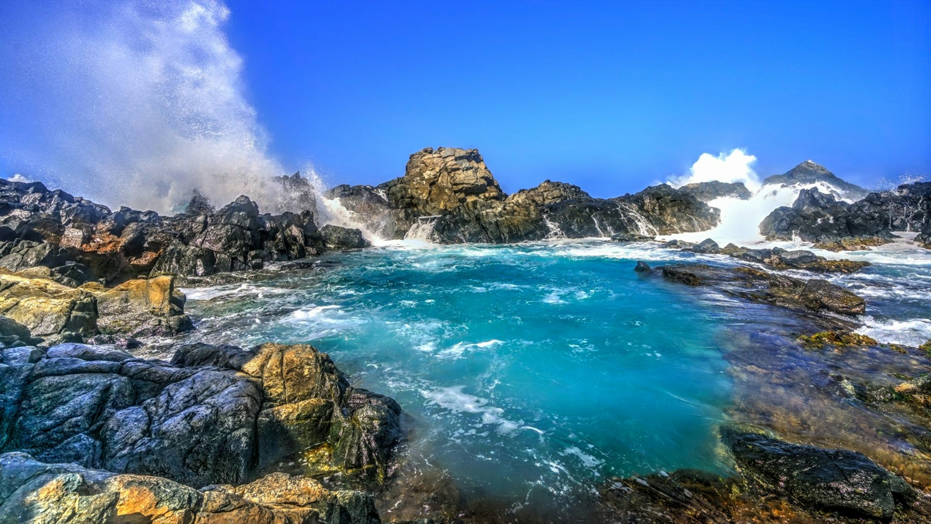 En våg slår mot klippan nära den naturliga poolen på Aruba © Chiragsinh Yadav / Shutterstock