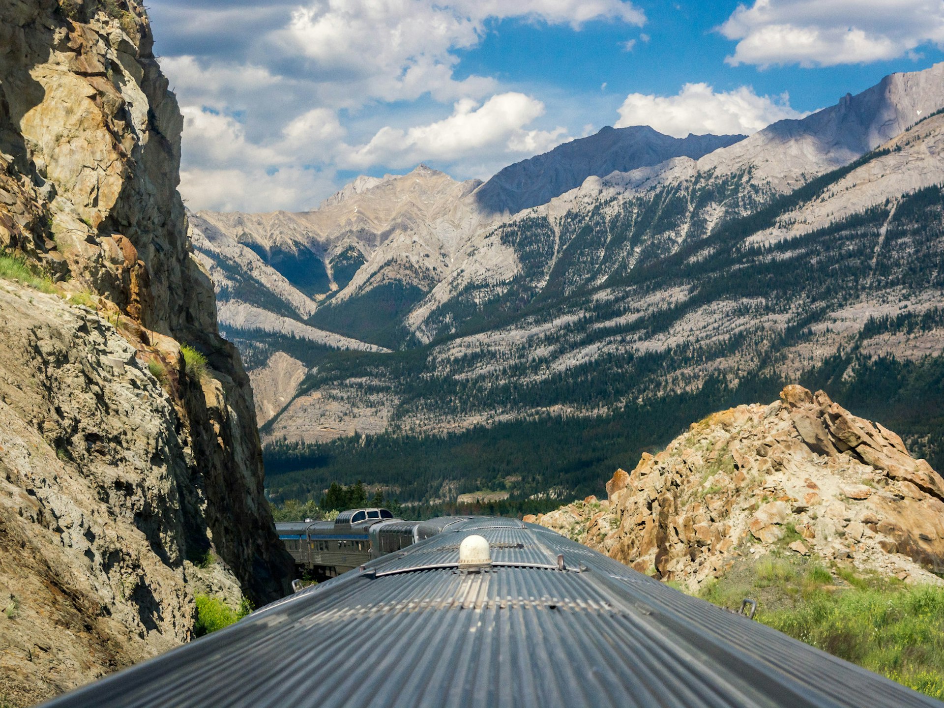 A shot from the roof of the train looking back at the carriages. The surrounding mountains are covered in forest