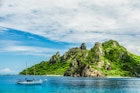 A sailboat in the water surrounding a green island in Fiji