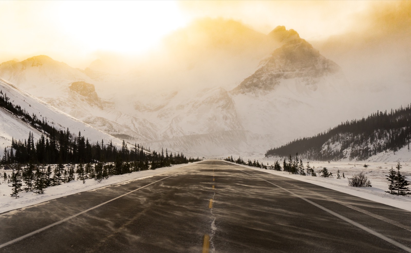 A snow-swept road is bathed in golden light as it appears to run straight into a mountain