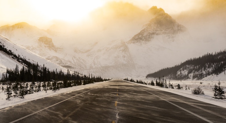 A snow-swept road is bathed in golden light as it appears to run straight into a mountain