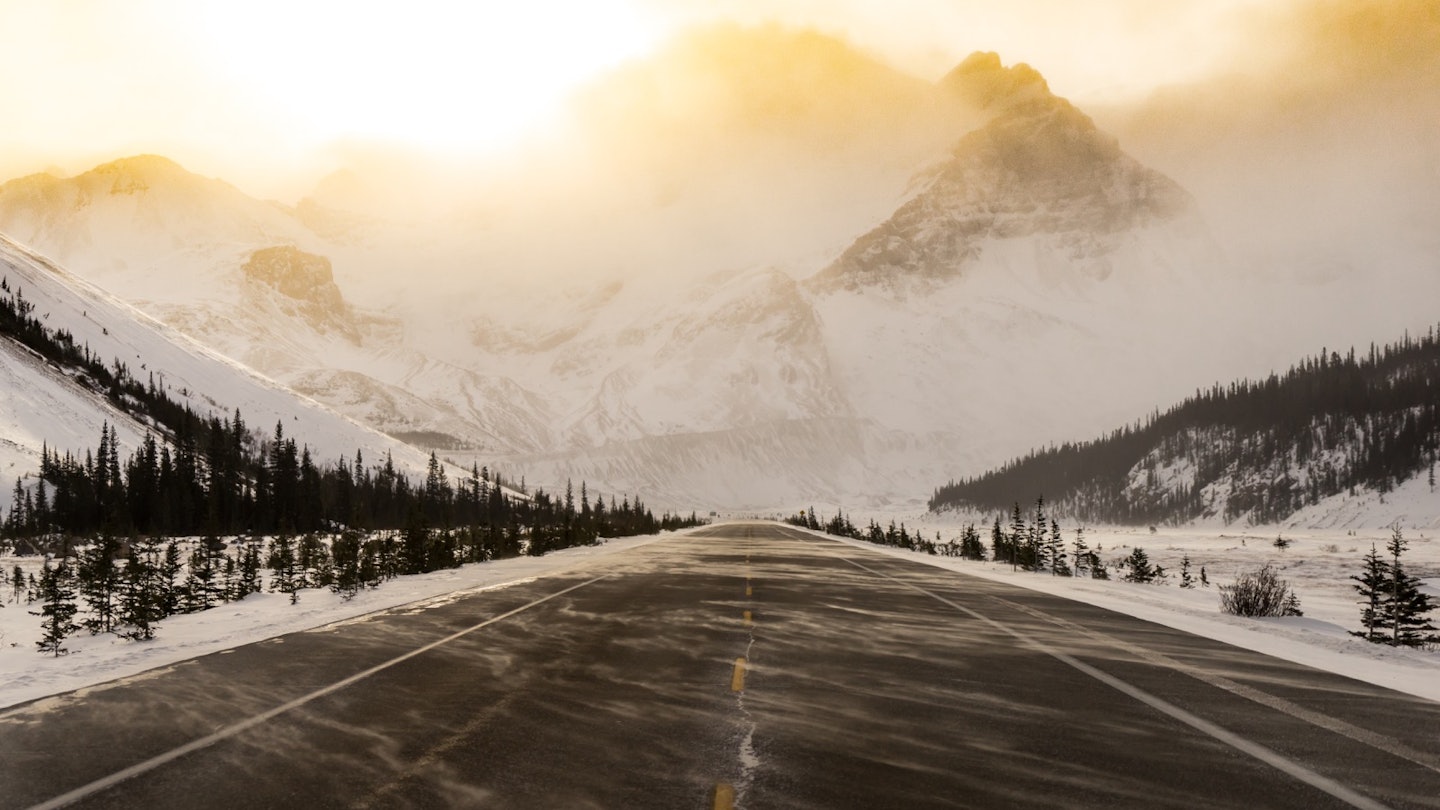 A snow-swept road is bathed in golden light as it appears to run straight into a mountain