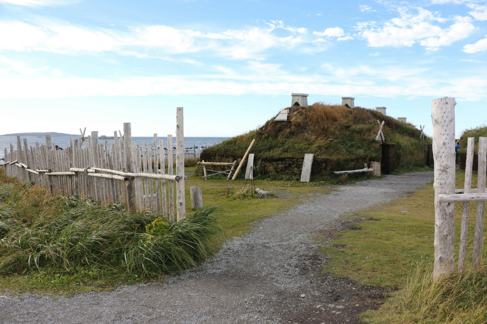 A Viking sod dwelling is circled by a white wooden fence in Western Newfoundland