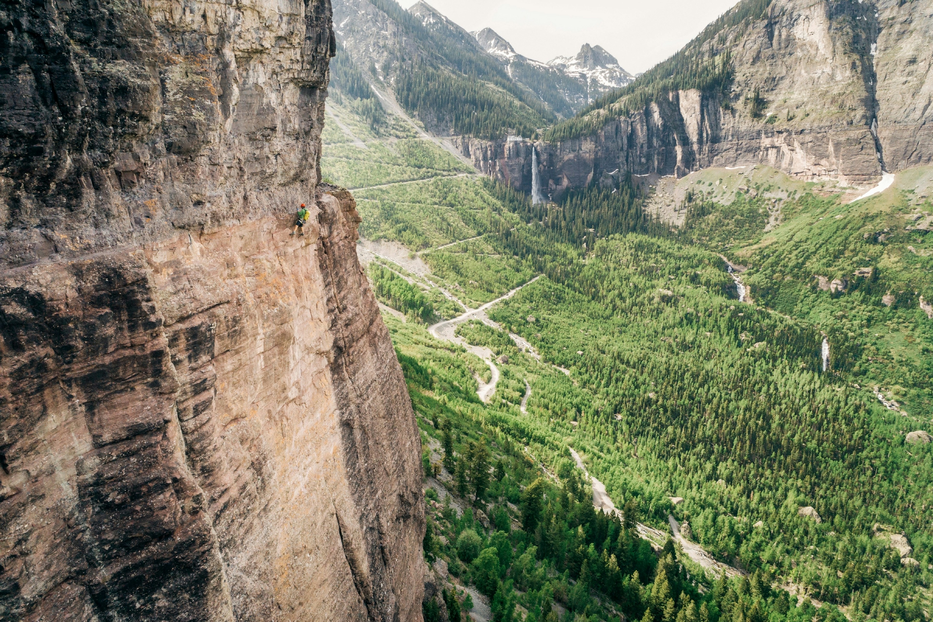 A man on the side of a cliff, crossing a via ferrata.
