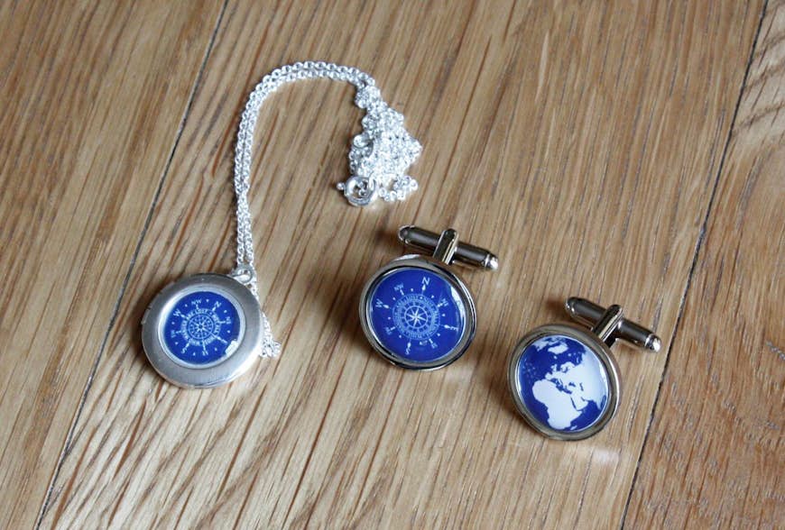 Cassiopis smycken med resetema, en medaljong med blå kompassdesign och ett par manschettknappar, en med kompassdesign och den andra med en karta över Europa