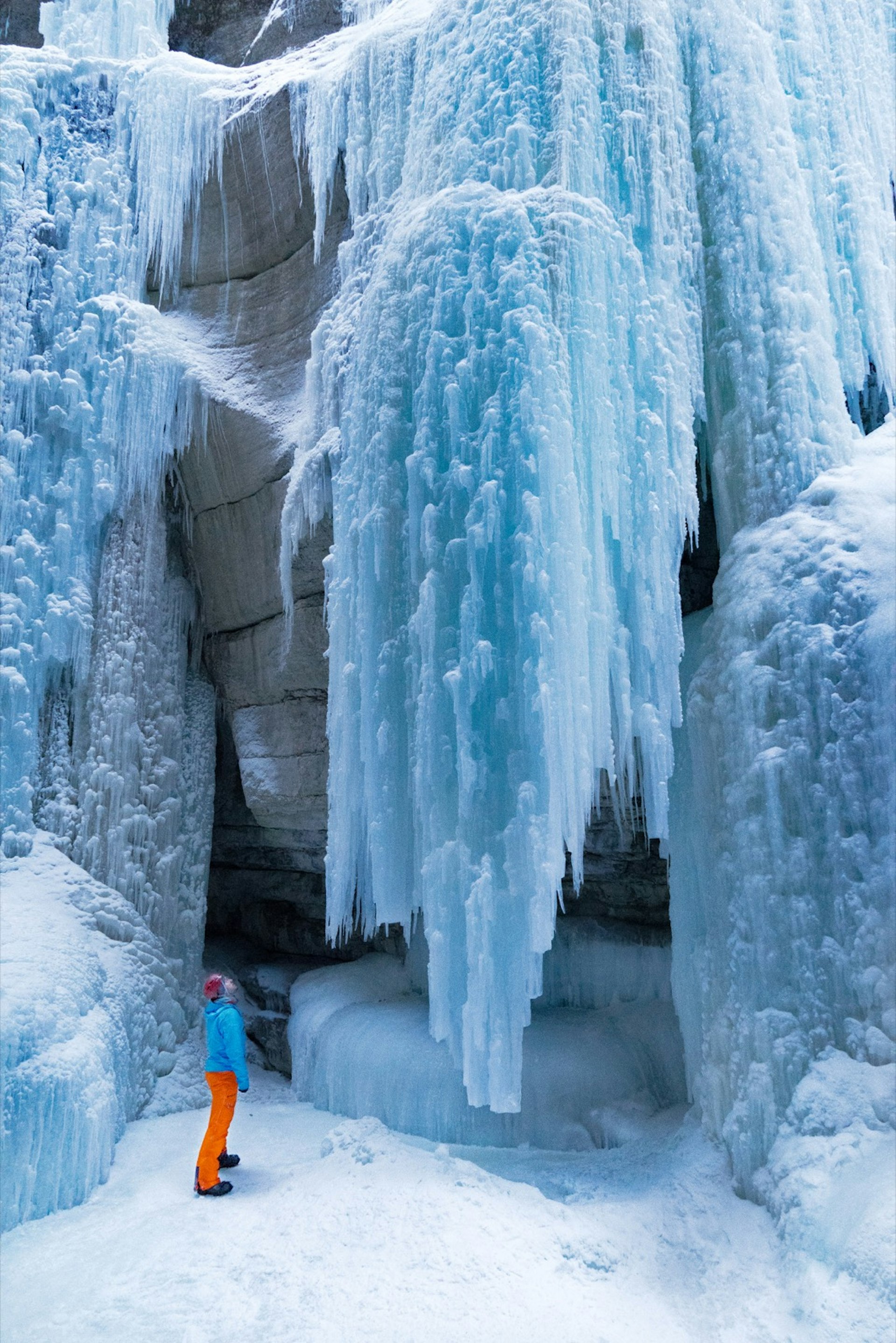 A very small looking person gazes up at a huge curtain of solid ice made from a frozen waterfall. Winter in Alberta Canada